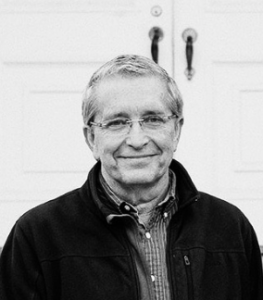 A man in glasses in front of a door. 