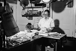 A black and white image of a man in a restaurant kitchen.