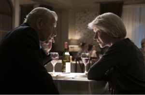 Ian McKellen as Roy Courtnay and Helen Mirren as Betty McLeish in New Line Cinema’s suspense thriller “The Good Liar.” Both actors are seated at a table looking each other inquisitively. 