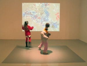 Camille's digital installation of colorful shapes projects on the wall. Children dance in front of it.