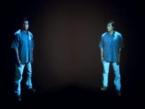 Film still from Gary Hill's "Standing Apart" Two identical men are facing each other.