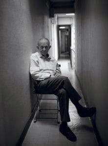 Frederick Wiseman sitting in a chair in a narrow hallway