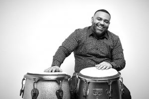 Nelson Bello smiling in front of drums.