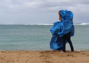 A standing figure on a beach is obscured by a blue tarp with the ocean in the background