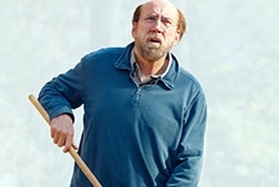 A man raking something in his yard looking up at the sky.