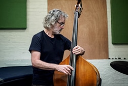 A man with gray hair and glasses playing the bass.
