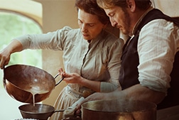 A man and woman cooking something in a kitchen.