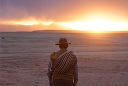 A man walking towards the sunset in the desert.