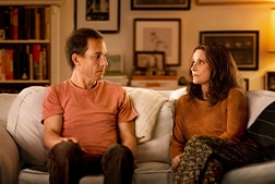 A man and a woman sitting on a couch looking at each other.