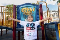 A young girl with her arms stretched wide wearing a tshirt that says Real Art Ways.