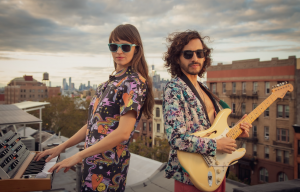 A man and a woman standing on a rooftop playing the keyboard and guitar.