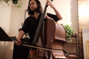 A man in glasses and long hair playing the cello.