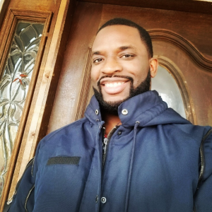 A man with a beard smiling in front of a wooden door.