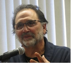 A man speaking into a microphone with glasses.
