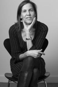 A black and white image of a woman sitting on a stool hunched over with her hand holding her chin.