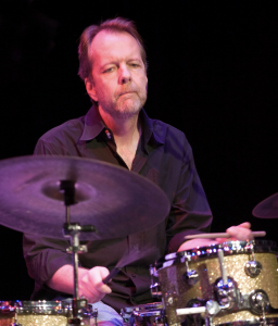 A man on stage playing a drum kit.