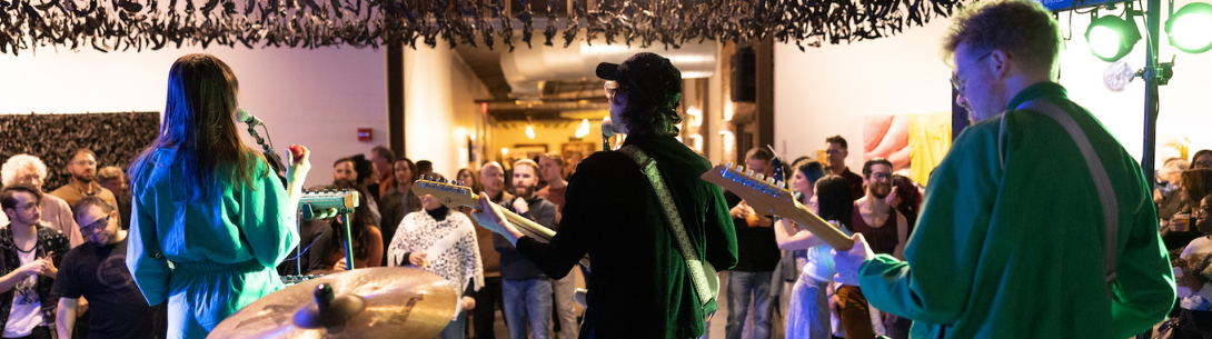 A band playing for a full crowd with bananas hanging from the ceiling.