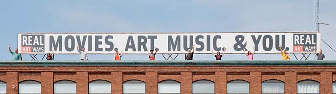 People standing on a building that says movies. art. music. and you.