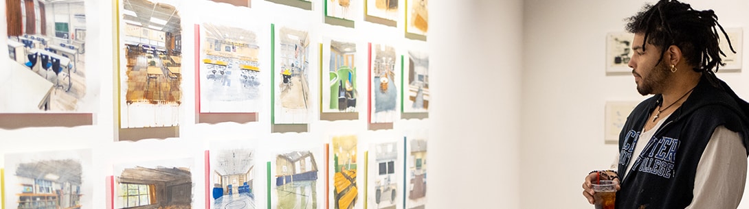 A man holding a drink and looking at artwork hung up on the wall.