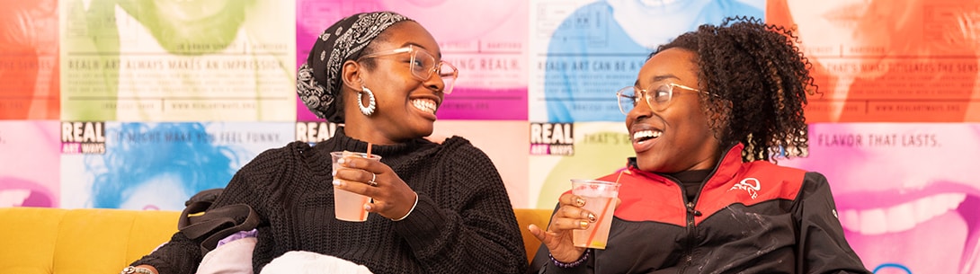 A group of two Black women enjoying a drink together with a colorful background.