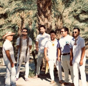 A group of men standing under a tree in the sun.