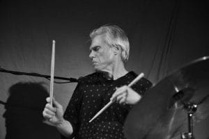 A black and white image of a man playing a drum kit.