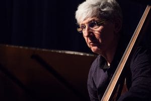 A man in glasses playing the bass on a darkly lit stage.