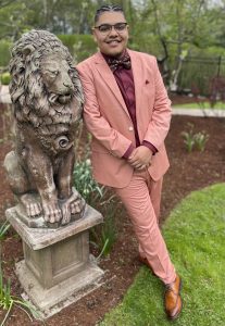 A man in a pink suite standing next to a statue of a lion.