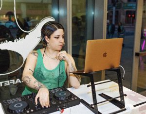 A woman behind a DJ booth looking at a laptop.