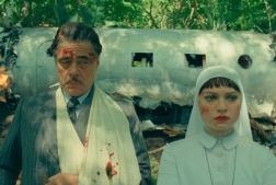 An injured man stands in front of a downed plane with his daughter, a nun