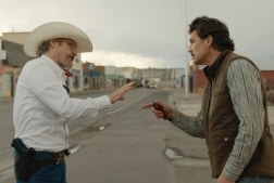 Two men stand off on a main street arguing and pointing fingers at each other